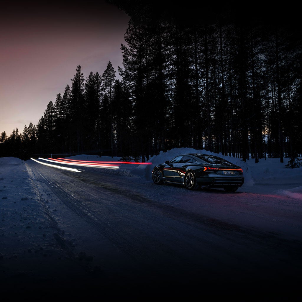 Long-exposure shot of an Audi RS e-tron GT driving on a snowy road at night, with light beams ahead.