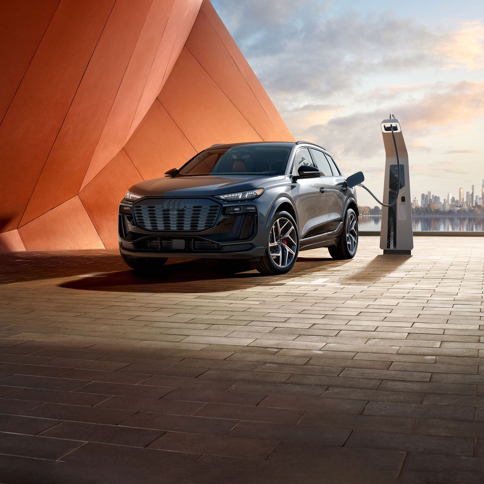 Vue de face de l'Audi SQ6 e-tron garée et en charge devant un paysage urbain futuriste.