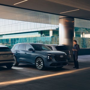 Depiction of a person using the Park assist pro feature via their cellphone, reversing an Audi Q7 in between two vehicles in a parking garage.