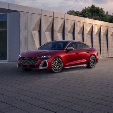 Three-quarter front view of the all-new Audi A5 parked by a modern building.