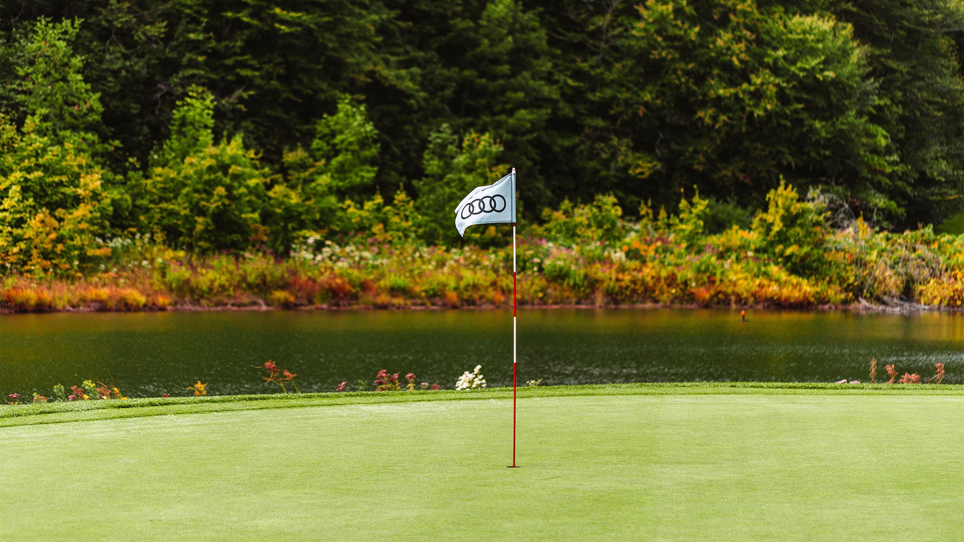 A flagstick with an Audi logo on a hole on a golf course.