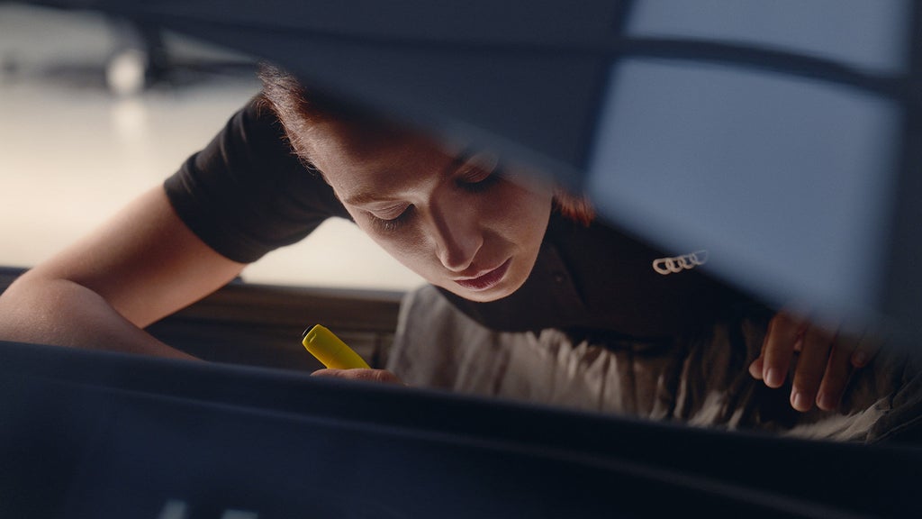 An Audi employee replacing parts under the hood of the vehicle.