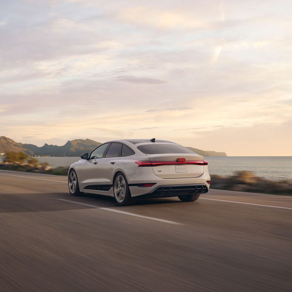 Vue de trois quarts arrière de l’Audi A6 e-tron accélérant sur une route au bord de l’eau.