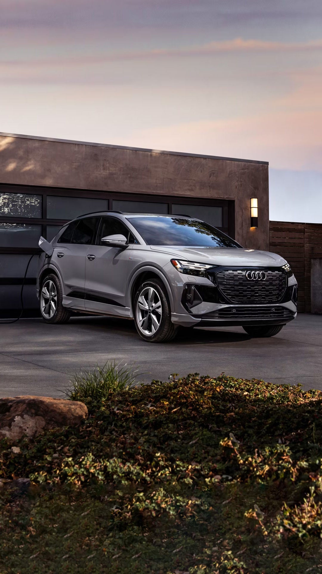 Three-quarter front-view of the Audi Q4 e-tron® charging in front of a person's home.
