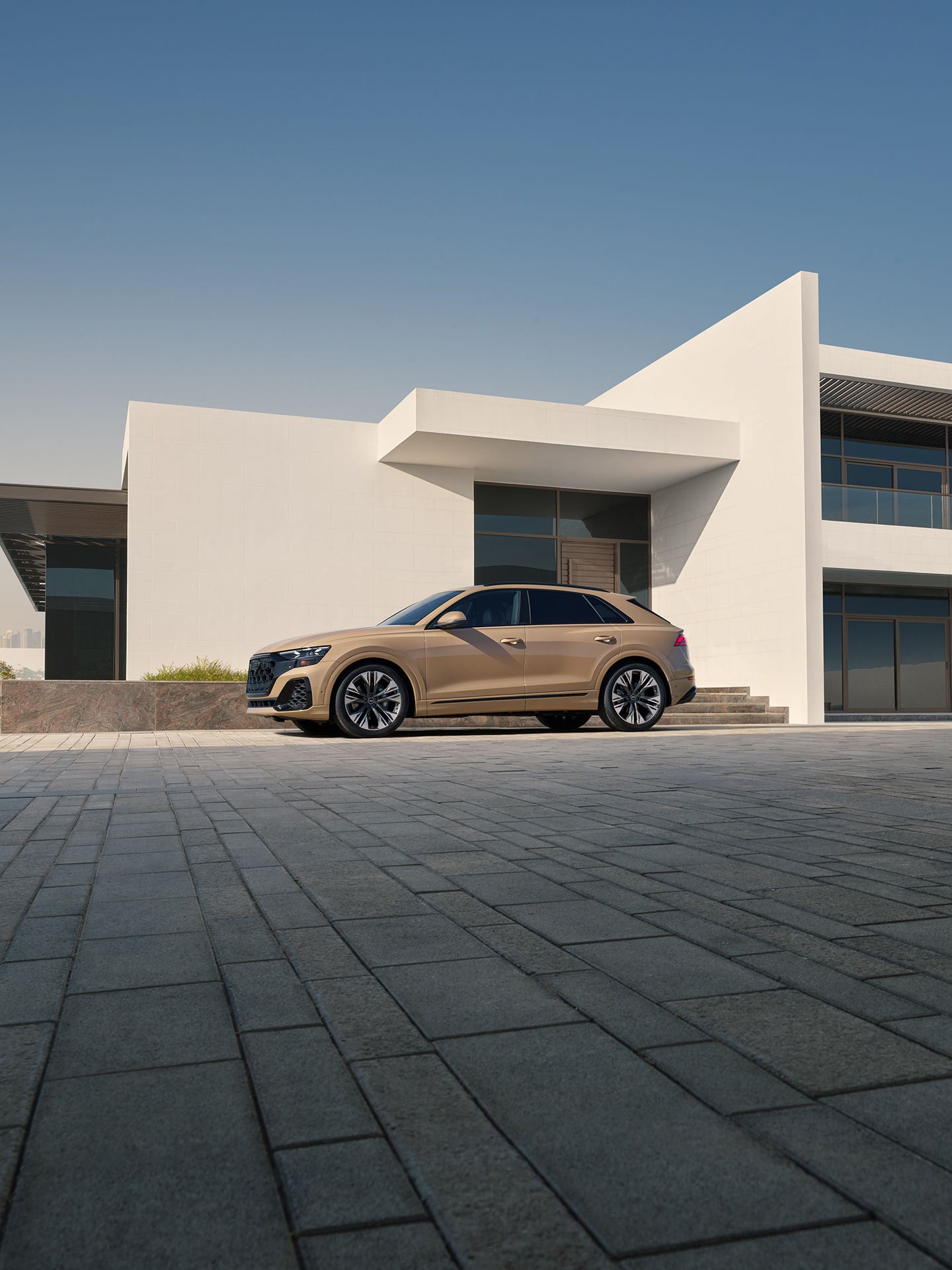 Elevated side view of the Audi Q8 parked in front of a modern house.