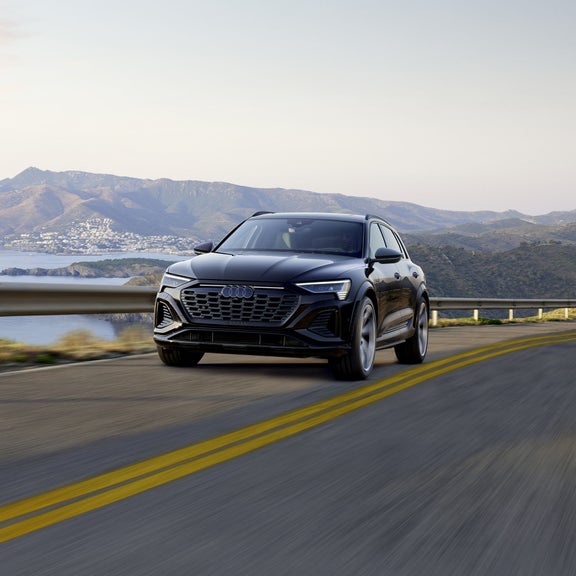 An Audi SQ8 e-tron driving down a road next to a body of water.