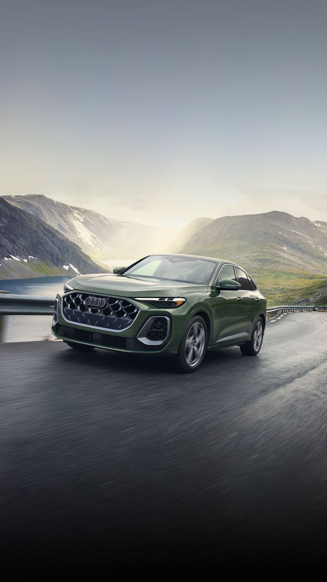 An Audi vehicle parked on an empty road with trees and hills in the background.