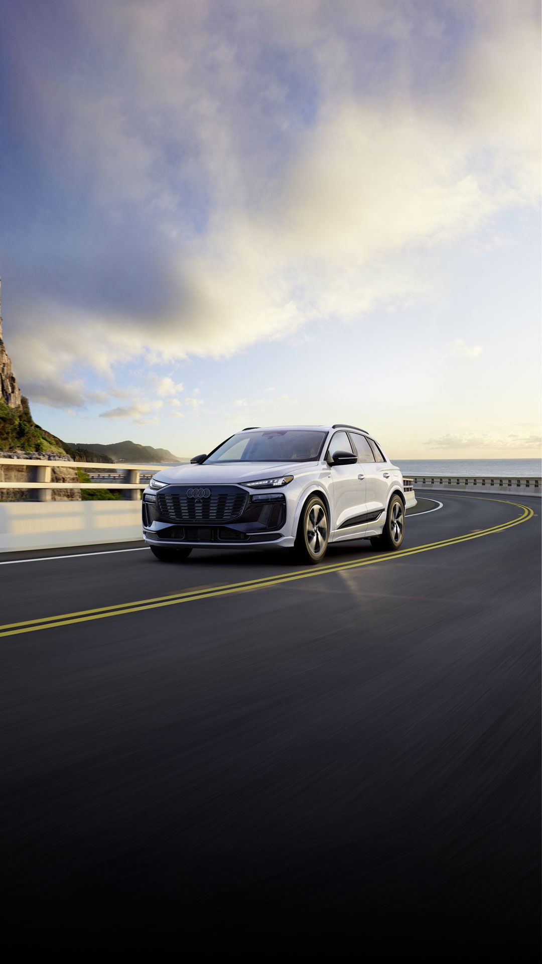 Three-quarter front view of the Audi Q6 e-tron accelerating on a hillside road.
