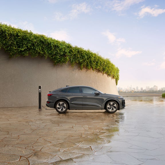 Vue latérale d'une Audi Q6 Sportback e-tron grise garée et en charge.