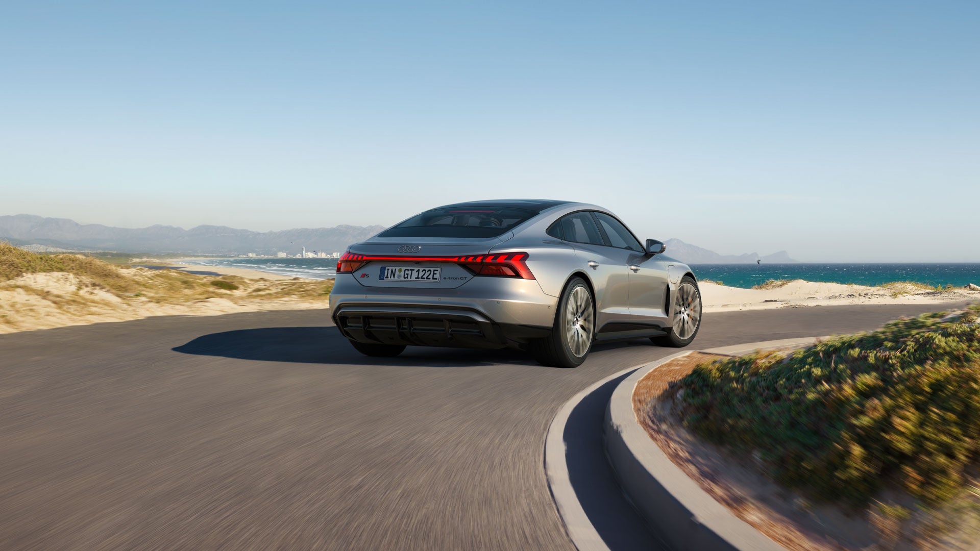 Profil latéral d’une Audi e-tron en recharge dans un stationnement près d’un plan d’eau.