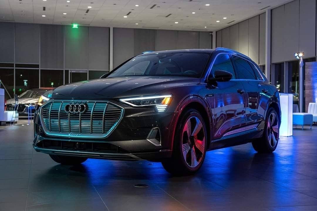 Audi sales specialist walking with a customer through the showroom. The sales specialist is handing the customer a key fob for an Audi vehicle.