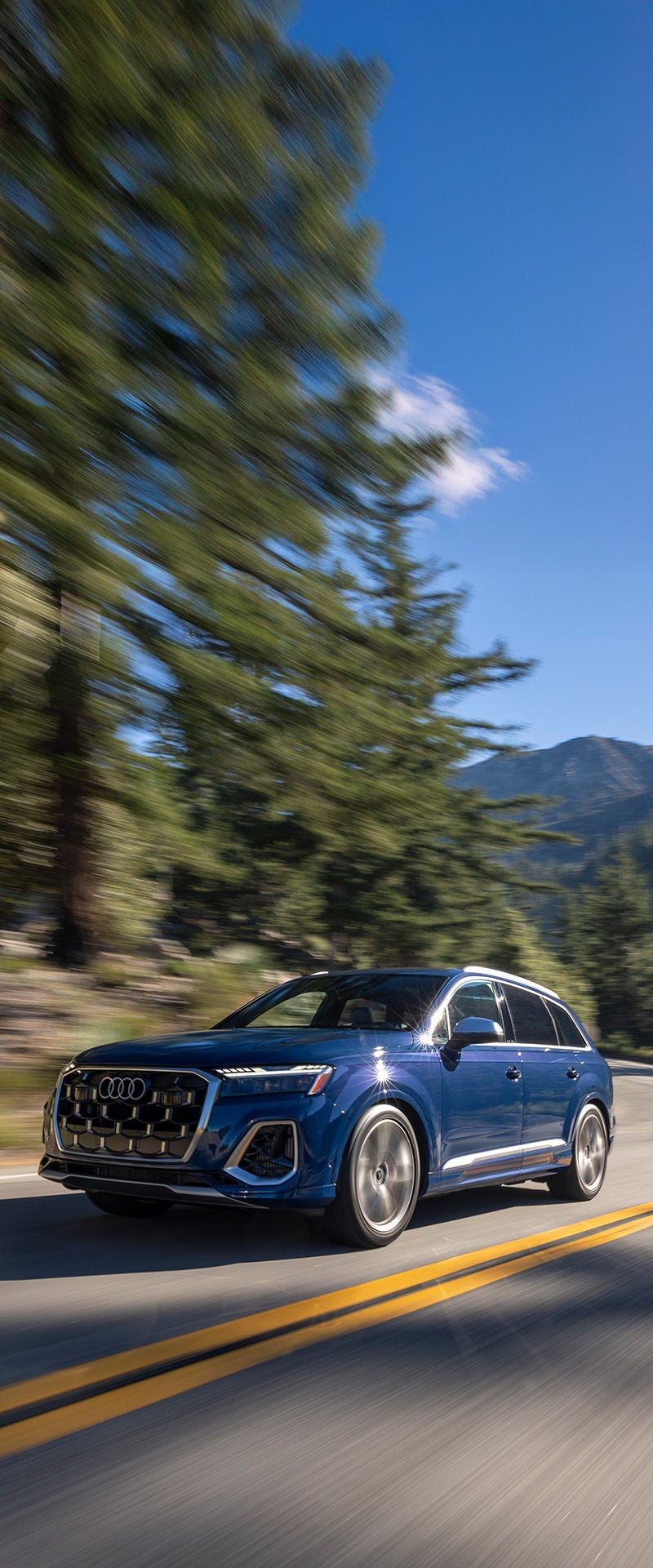 Blue 2025 Audi Q7 driving fast through mountains with the background blurred