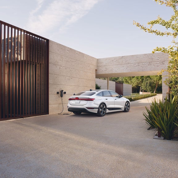 Vue de trois quarts arrière de l'Audi e-tron garée et en charge près d'une maison moderne.