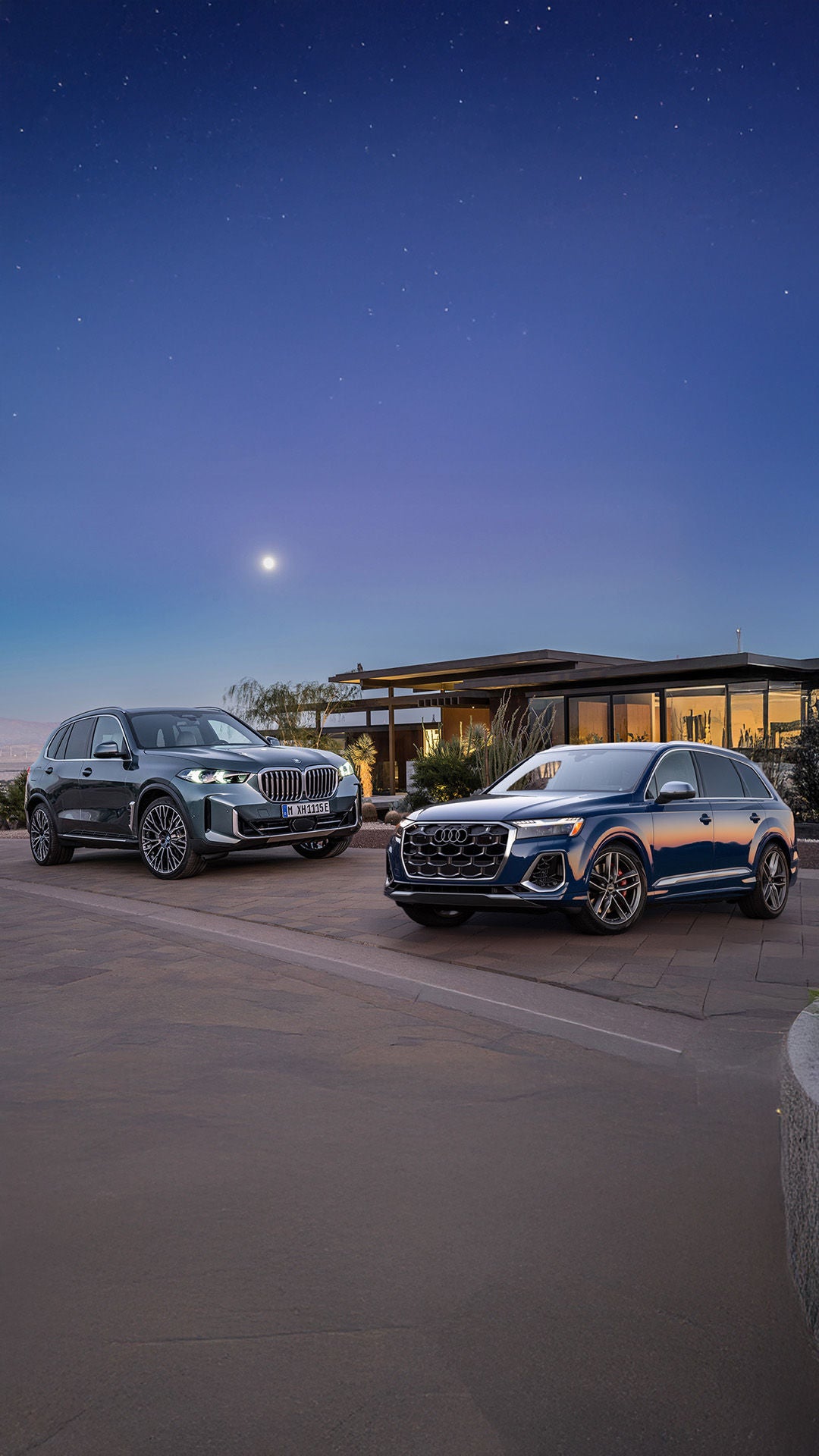 2026 Audi Q7 and BMW X5 parked infront of a mondern house under a star filled sky