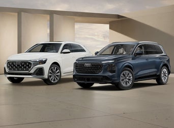 2027 Audi Q8 Premium 55 in Carrara White and Q7 Premium in Alopias Blue Metallic, posed in a modern architectural space.
