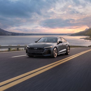 Three-quarter front view of the Audi A5 in motion on a waterside road.