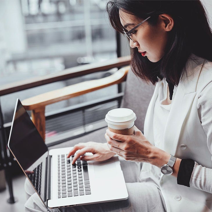 A woman dressed in business attire uses her laptop at a café.