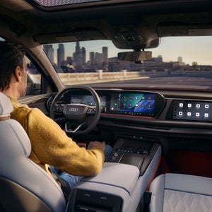 Close-up of a display in the vehicle interior. The silhouette of a vehicle travelling straight ahead is shown. To the left is a text box providing information about assisted hands-free driving.