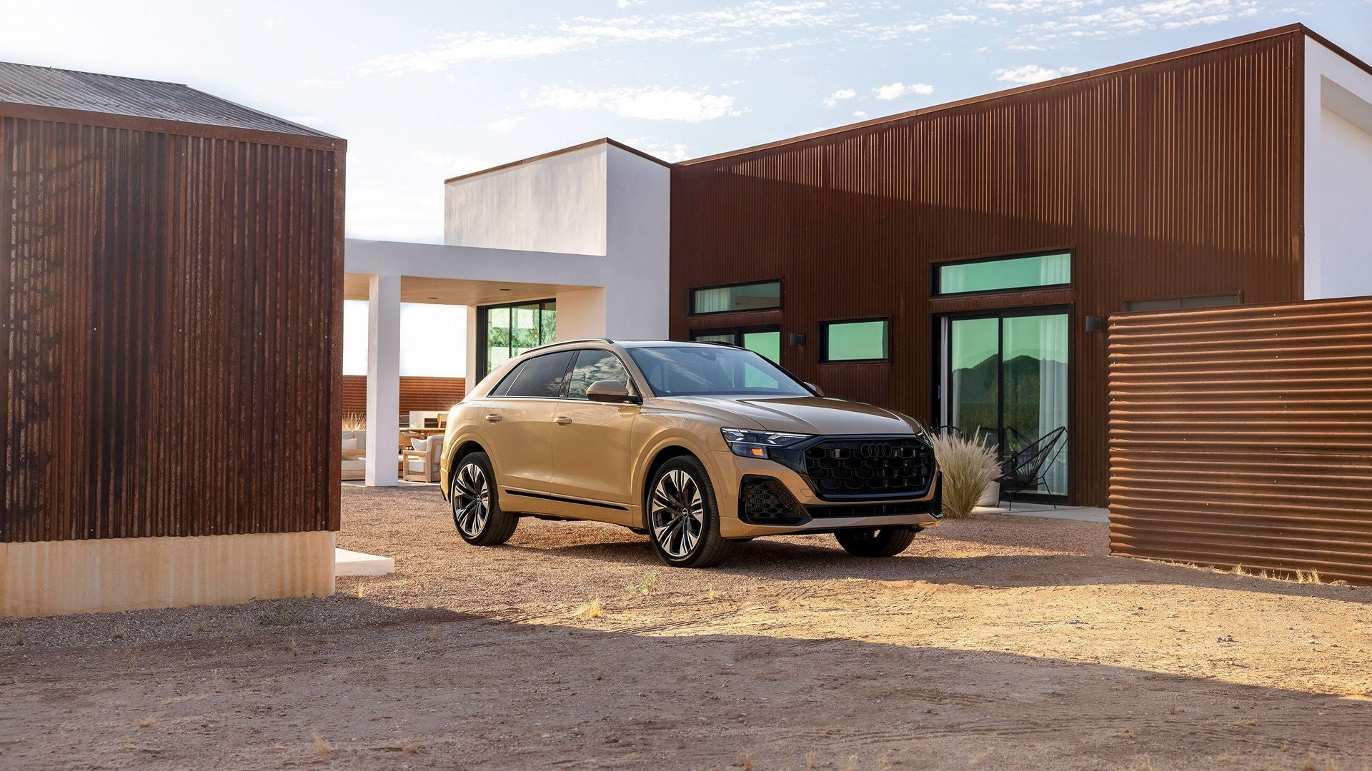 Light gold Audi Q8 parked outside on gravel, in from of a modern home. 