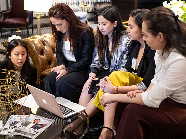 A group of women sitting on a couch, working on a project together.