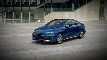 Front three quarter of the Audi S3, parked in front of a modern building.