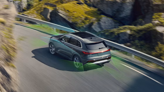 Gray Audi SQ5 driving fast on an open road with rocks and vegetation around. 