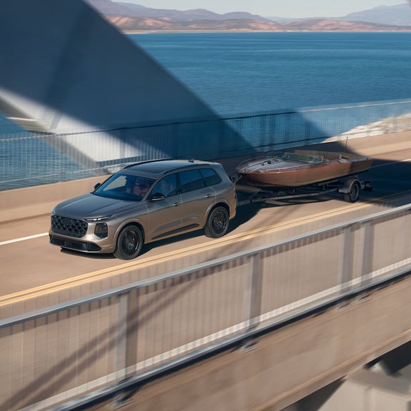 The Audi SQ7 SUV, viewed from the front at an angle on a bridge. The vehicle is towing a trailer loaded with a motorboat.