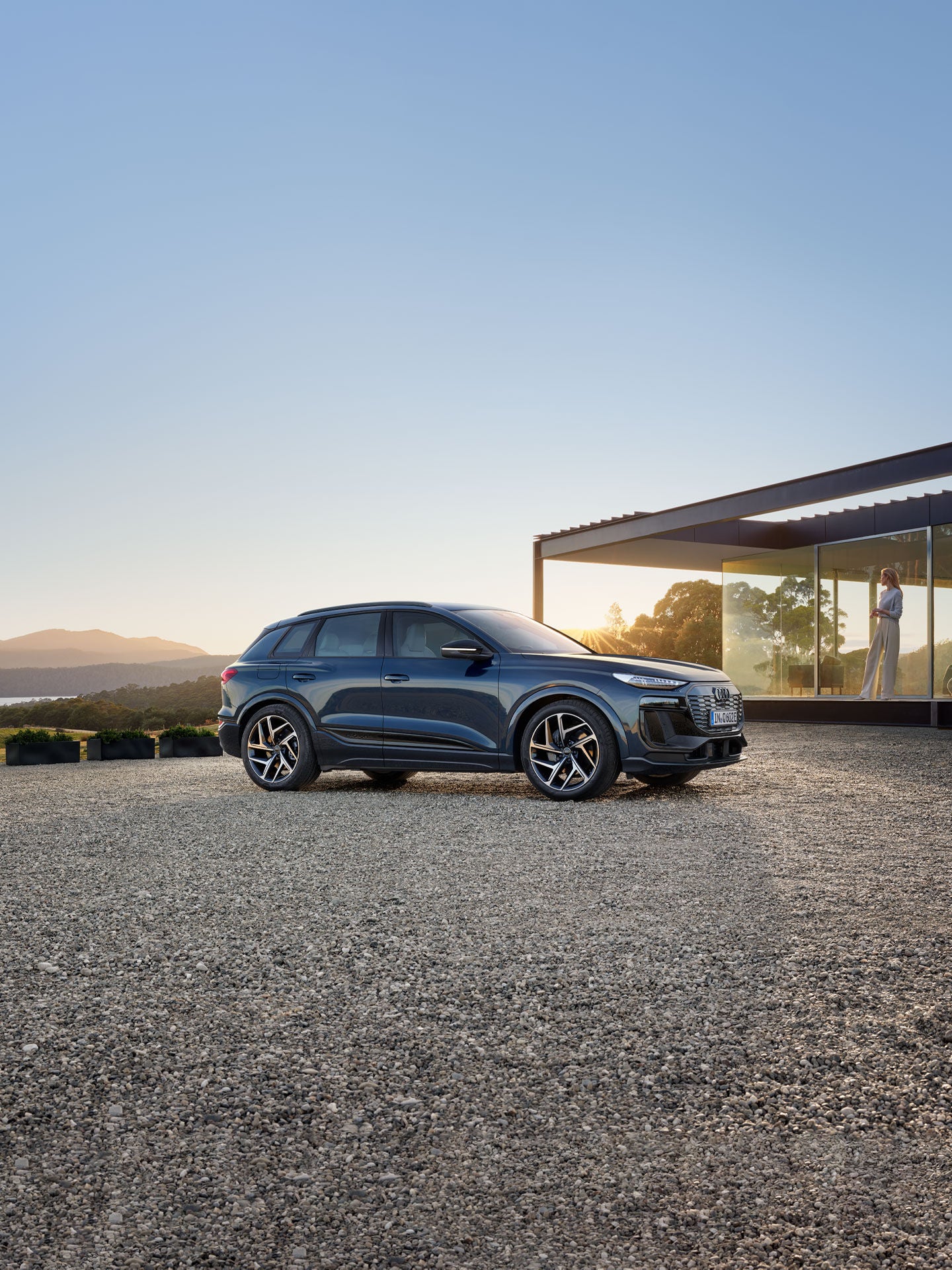 Vue de trois quarts de l’Audi Q6 e-tron à côté d’une maison de style moderne.