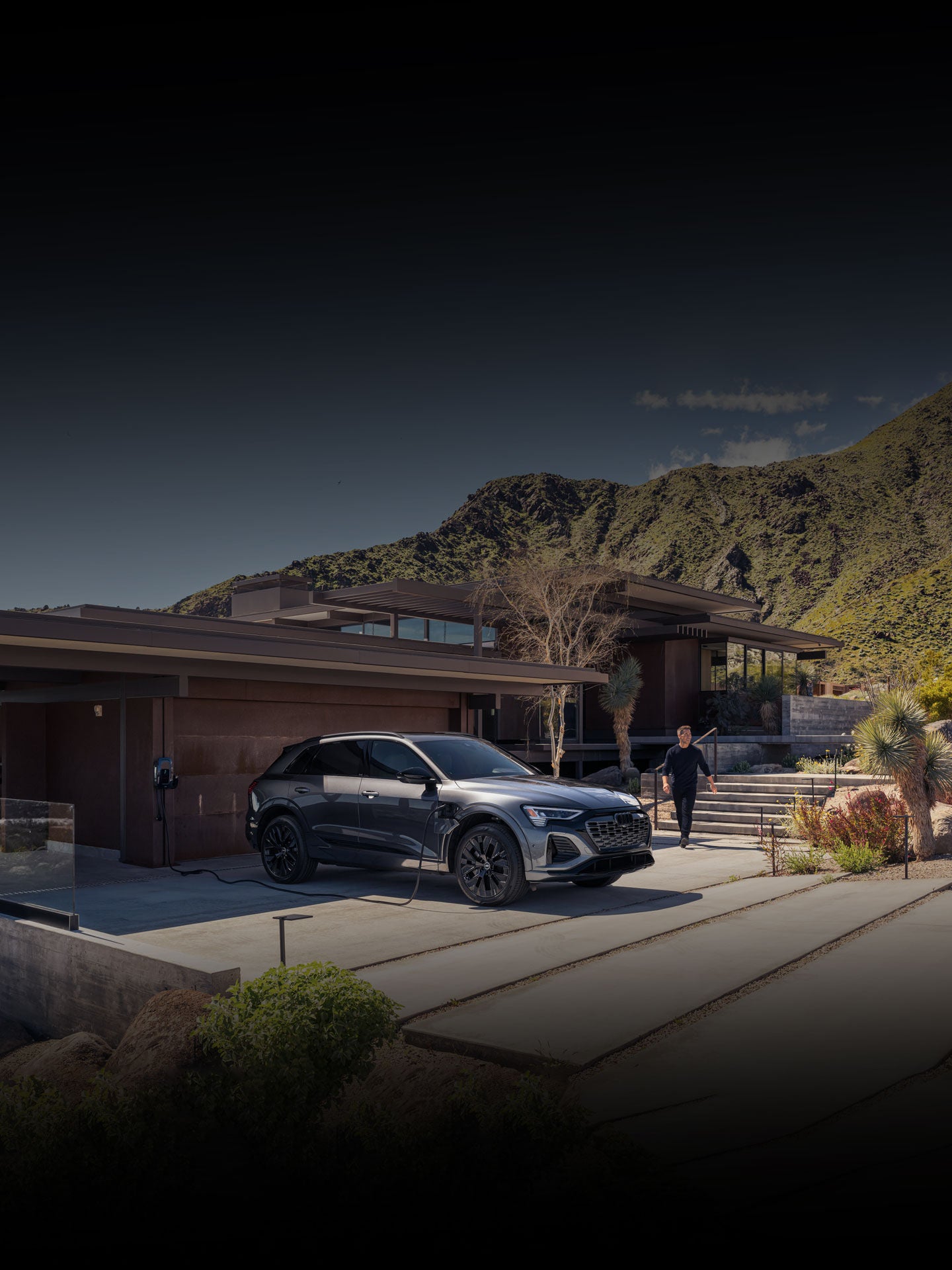 A man approaching his black Audi Q8 e-tron as it charges in front of a modern building. 