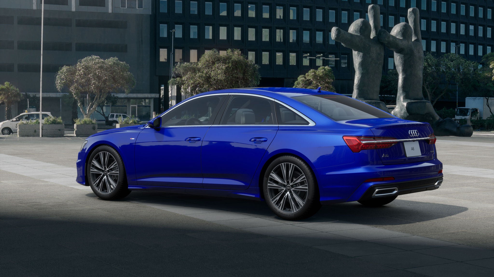 A blue Audi A6 parked on a tiled road, near city buildings and a city street.
