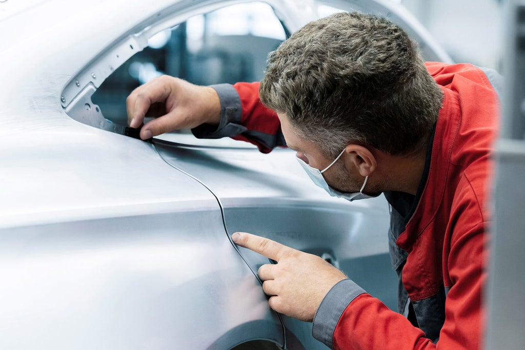 An Audi technician leaning over the frame of an Audi e-tron GT, using his hands to check for accurate gap dimensions.