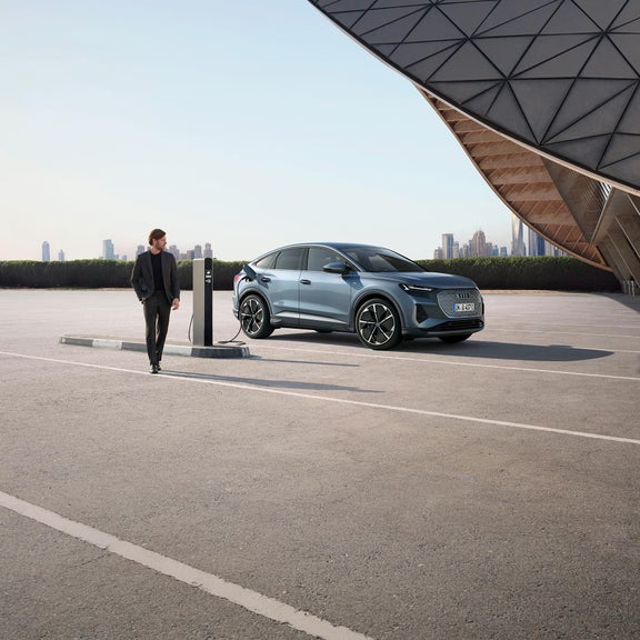 Photo d’un homme près de son Audi Q4 e-tron branché à une borne de recharge publique.