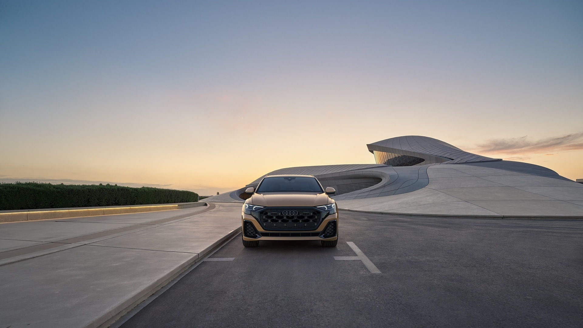 Audi Q8 vehicle parked on concrete ground with a modern, concrete background with green landscaping on the side.