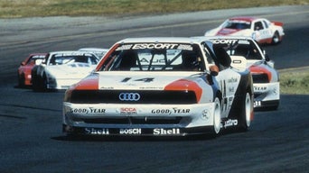 Front-view of Audi racing vehicles winding on a racetrack.