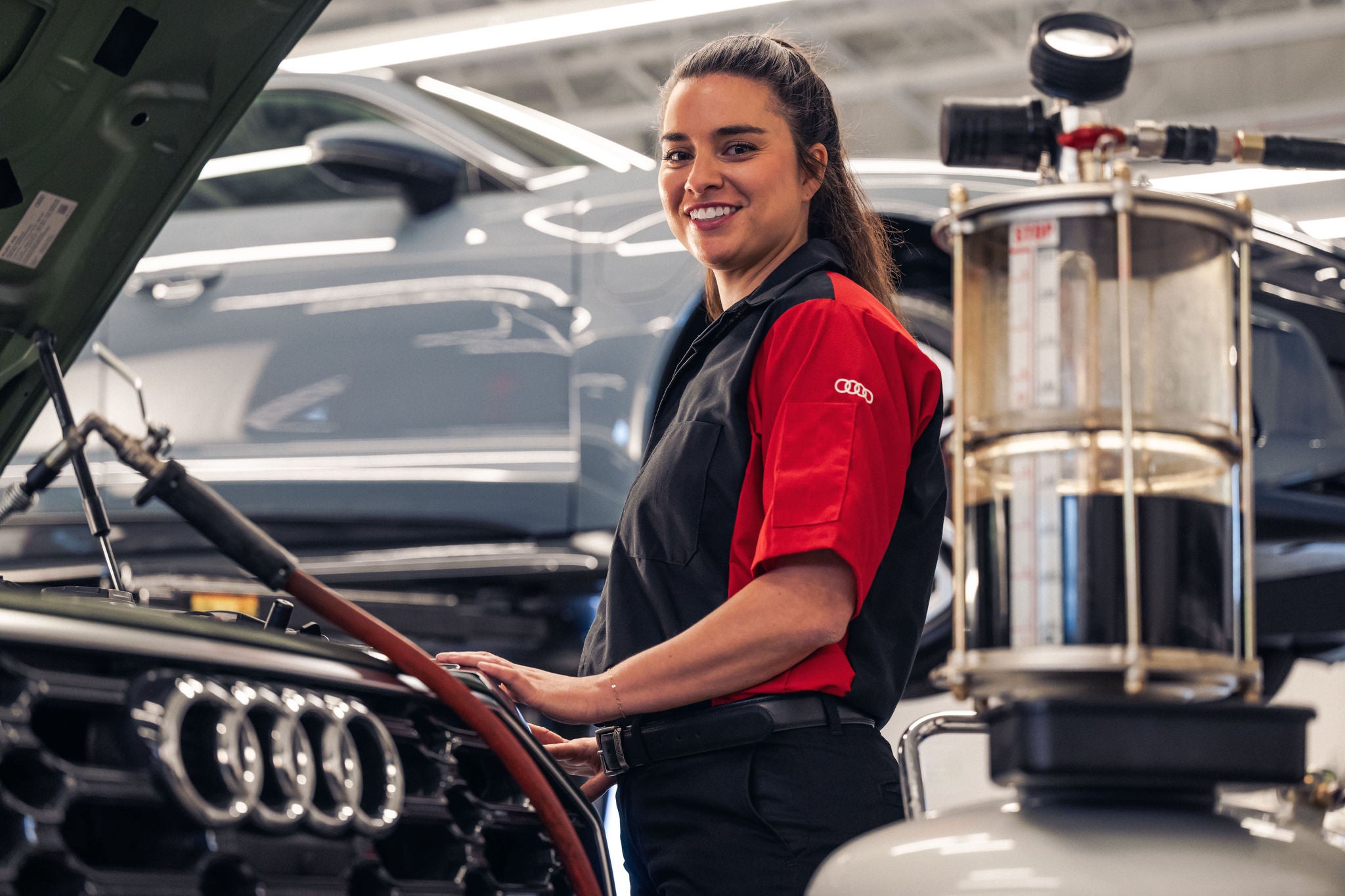 Service technician smiling while standing at the front of an Audi's open hood.