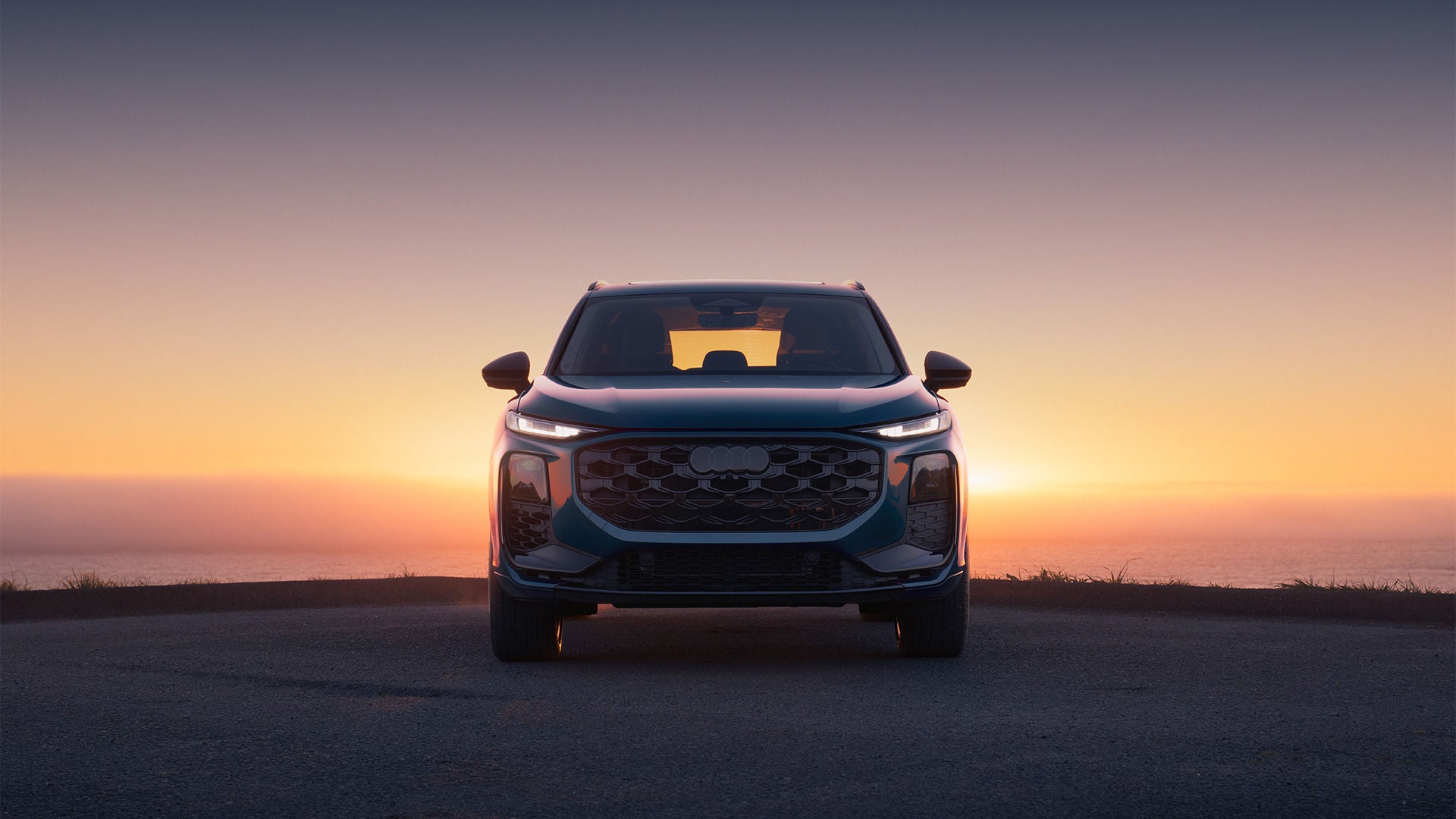 Front view of an Audi Q3 with a sunset in the background.