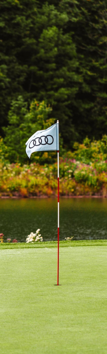 Close-up photo of an Audi golf flag on the green of a golf course.