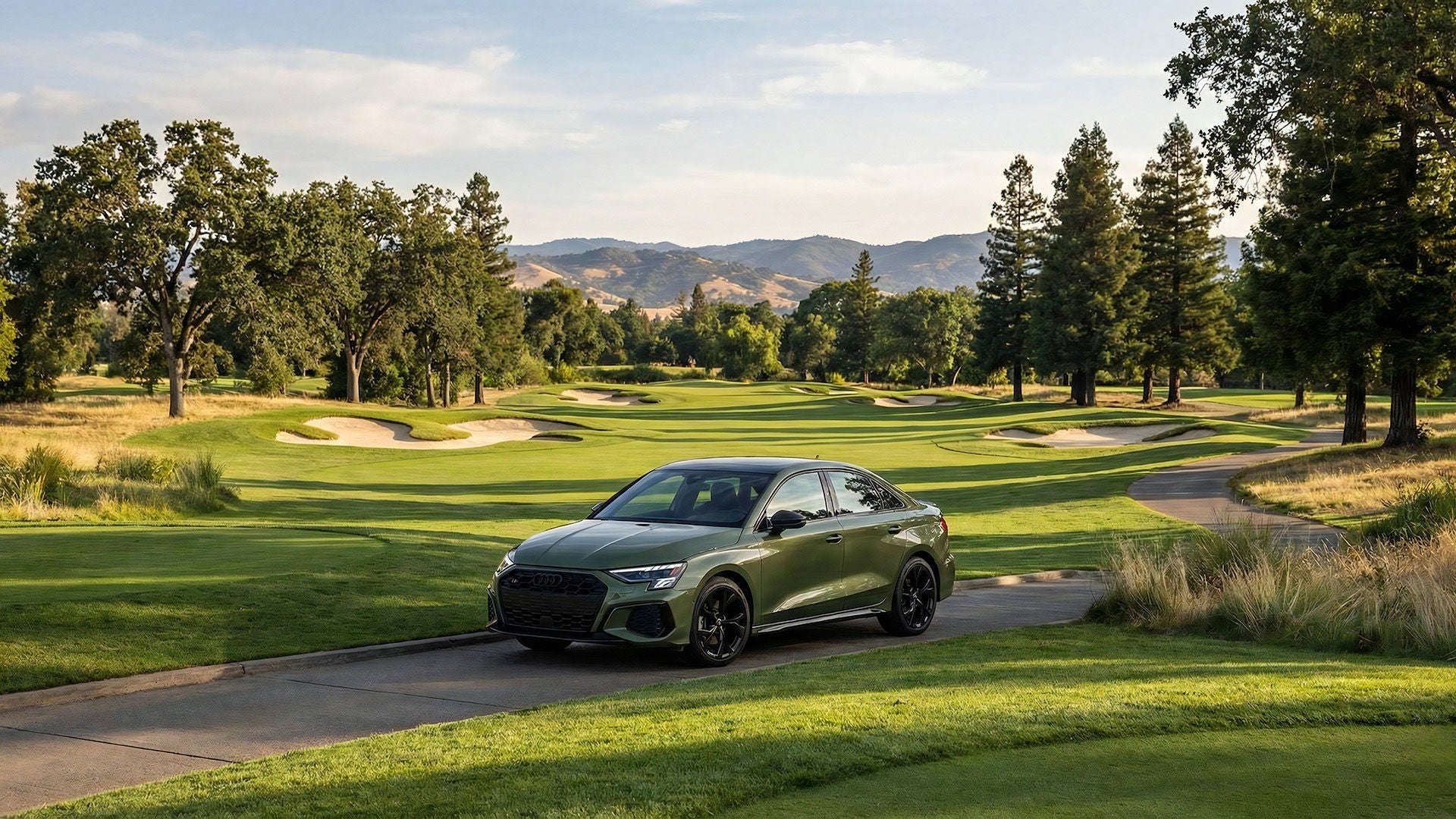 A green 2026 Audi A3 parked next to a golf course lined by pine trees with mountains in the background
