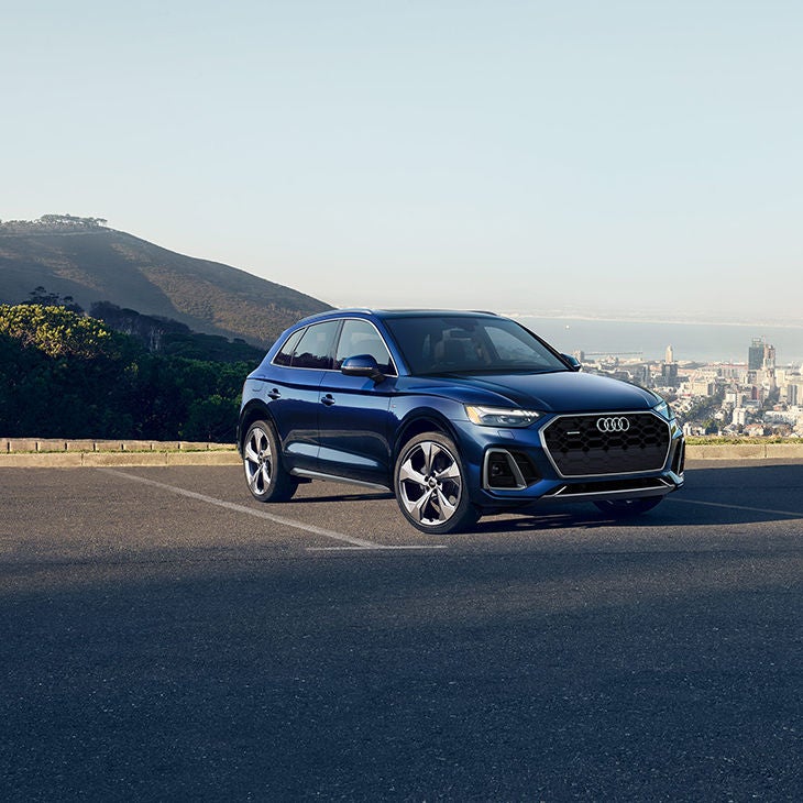 A blue Audi Q5 in an empty parking lot, overlooking city buildings and a lake. 