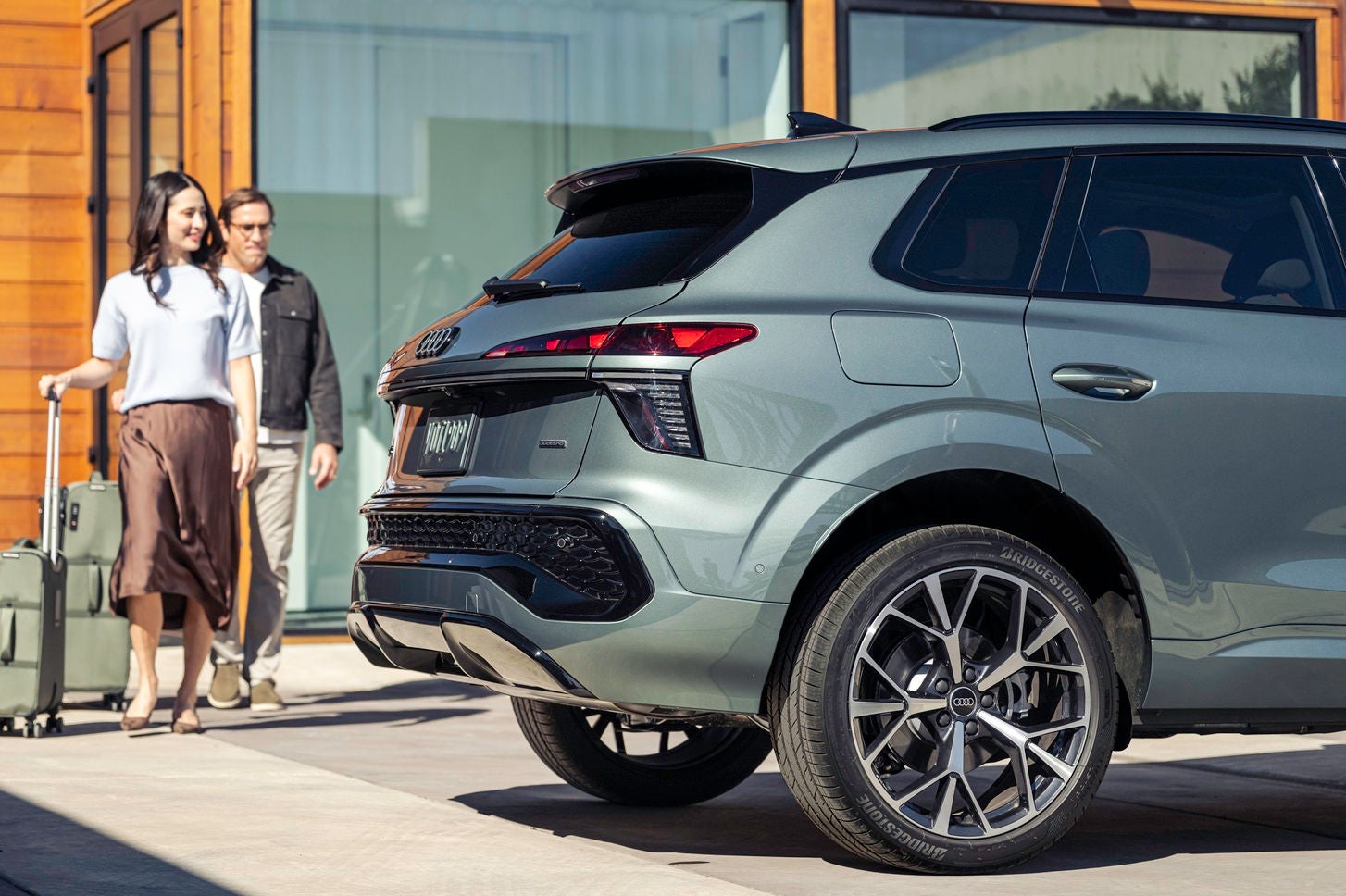 An Asian couple walks to their grey Audi Q3 with luggage in tow.