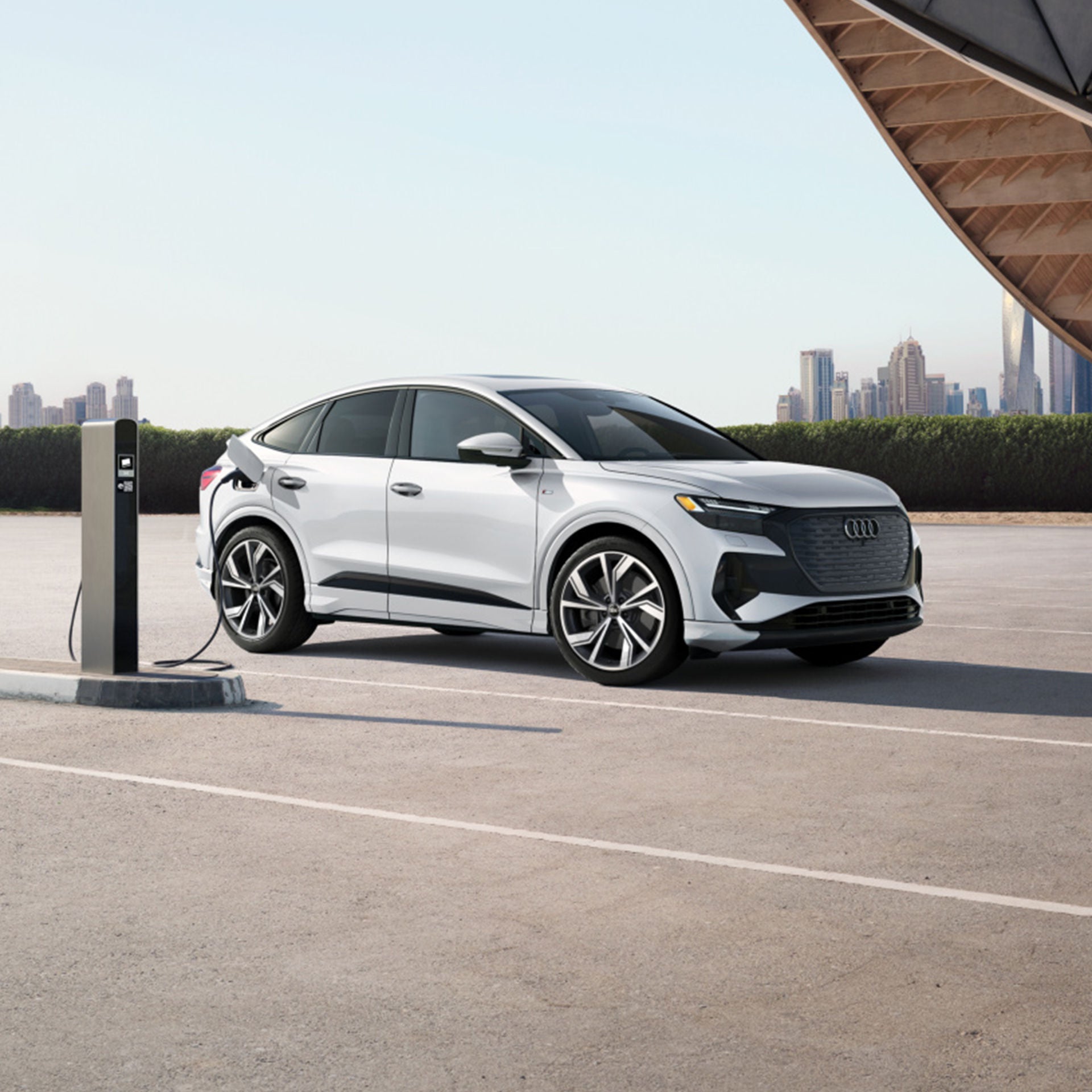 Vue de trois quarts avant d’un Audi Q4 Sportback e-tron blanc en recharge avec une ville en arrière-plan.