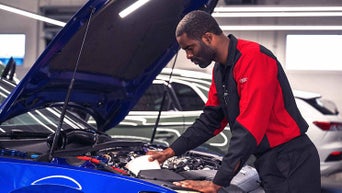 Service technician servicing vehicle with hood open.