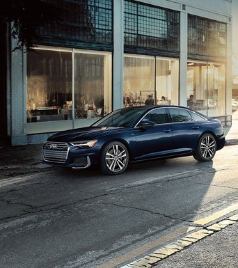 An Audi A6 parked on the street, near a building that is home to a busy cafe. 