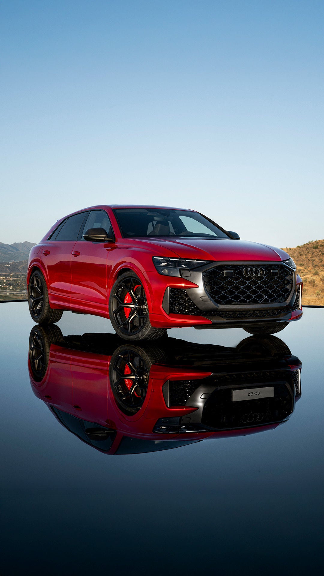 2025 Audi RS Q8 in red parked on water with reflection of the SUV and desert mountains in background