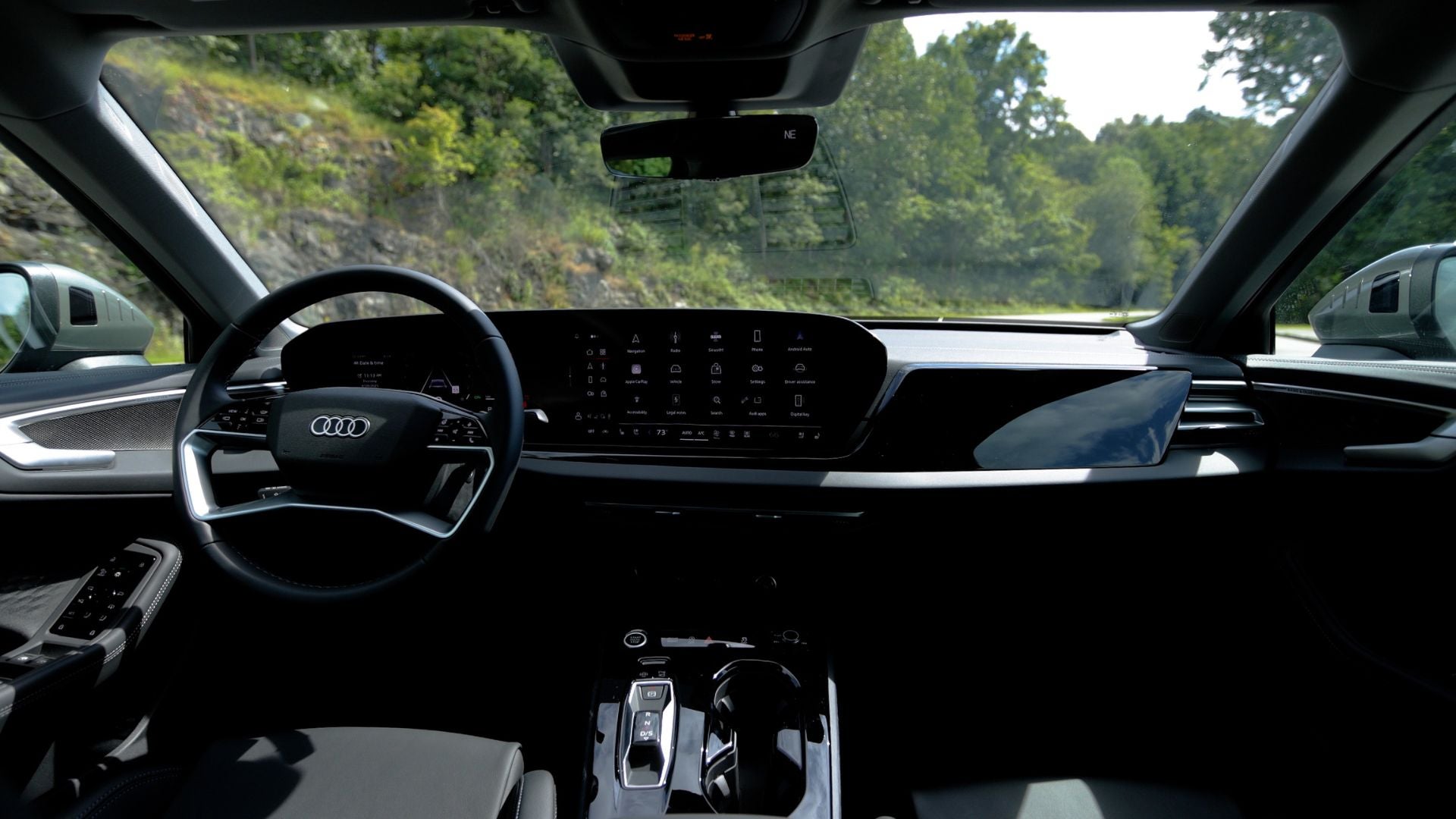 All black interior of an Audi A5 sedan. There are trees visible out of the front window.