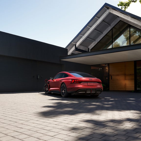 Three-quarter rear view of the Audi RS e-tron GT parked on a driveway of a modern home.