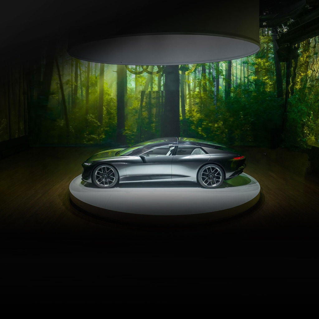  Profil latéral de la voiture conceptuelle Audi grandsphere, stationnée sur une scène intérieure, devant la projection d’une forêt.