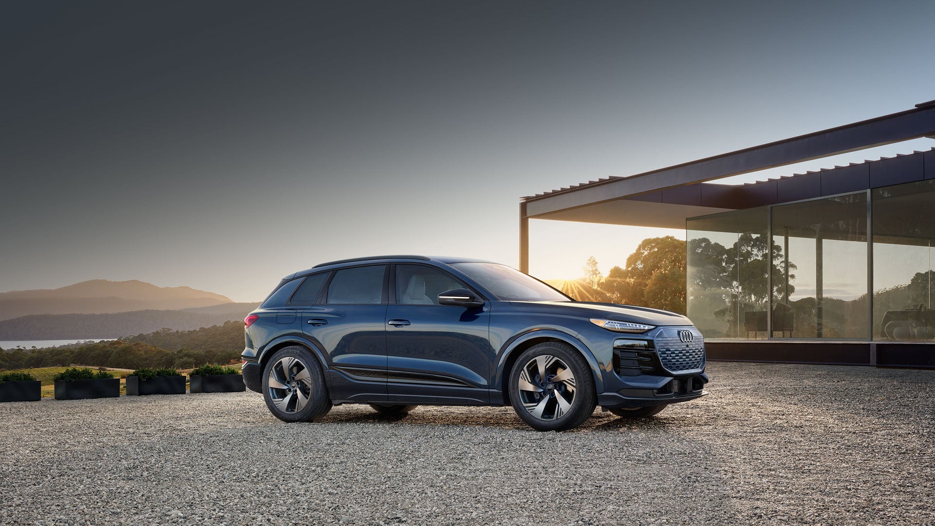 Image of an Audi Q6 e-tron parked in front of a glass house