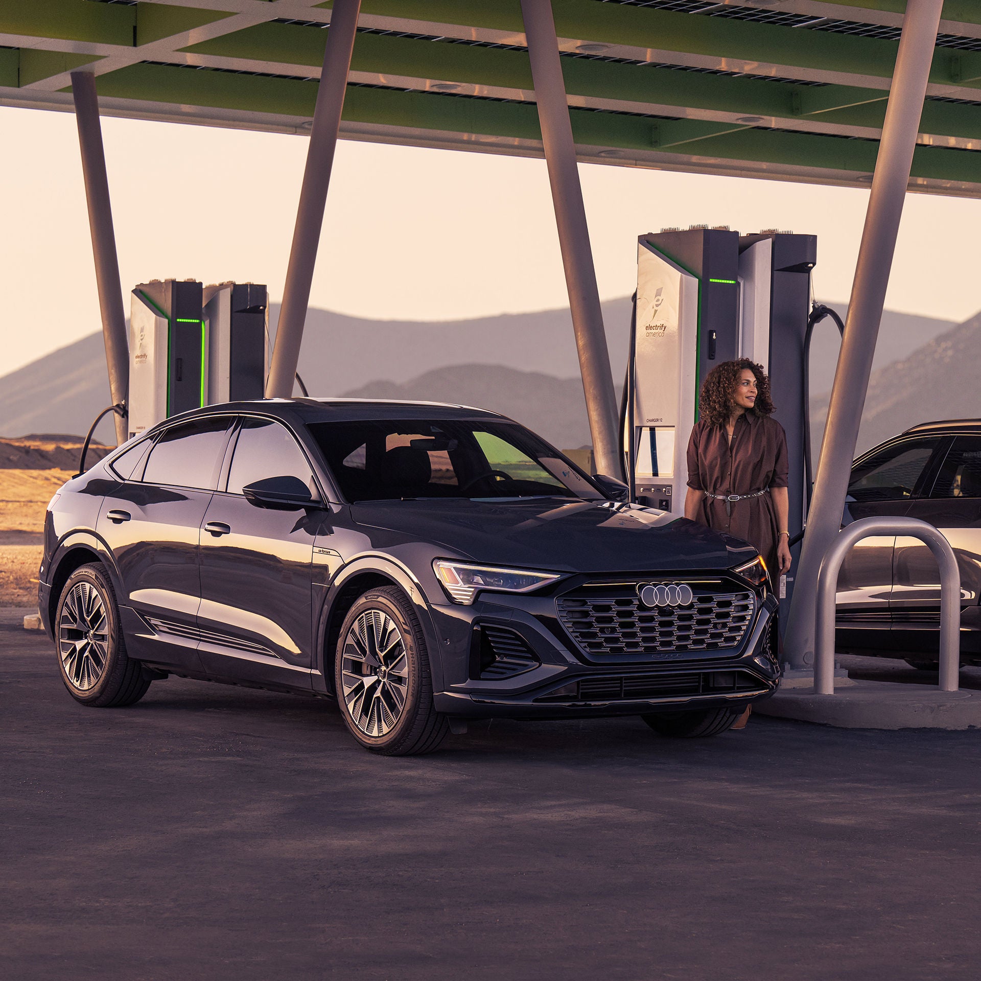 A woman charging her Audi Q8 e-tron at an Electrify America charging station. 