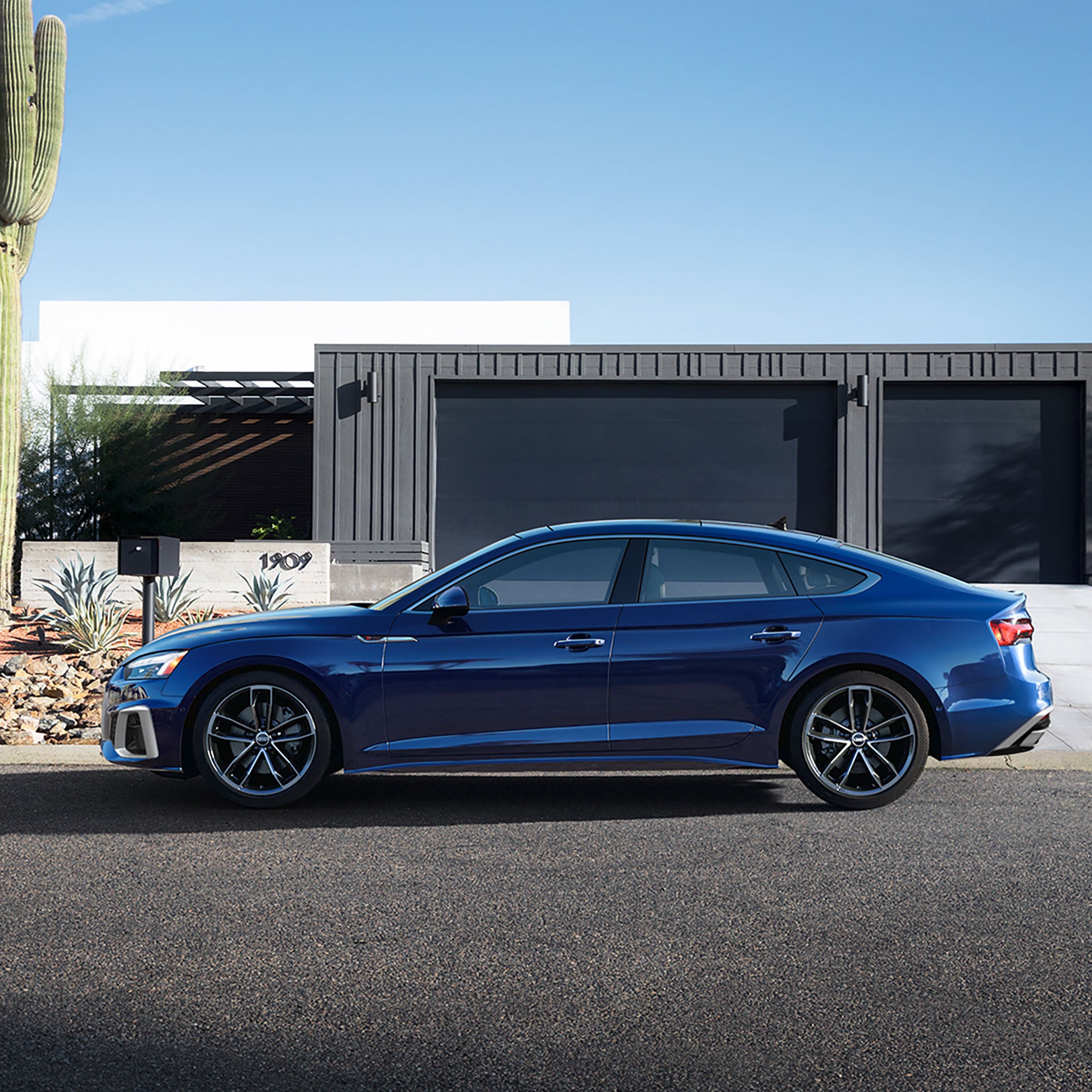 Side profile of the Audi A5 Sportback parked in front of modern house.